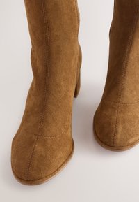 Braune kniehohe Stiefel aus Wildleder mit abgerundetem Zehenbereich und Reißverschluss an der Seite, mit tonalem Stichmuster und stabilem Blockabsatz.