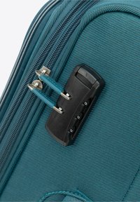 Zbliżenie na turkusową torbę z materiału pokazującą zamki błyskawiczne oraz czarną blokadę szyfrową z niebieskimi uchwytami, podkreślające teksturowaną powierzchnię i bezpieczne zamknięcie.