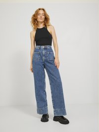 Svart ermeløs topp kombinert med høyhåndte, vide blå denimbukser med store lommer og rullet kant. Svart klumpete sko fullfører antrekket.