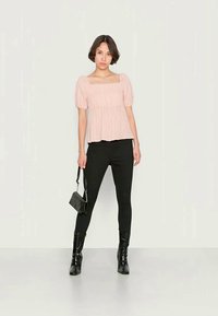 Blusa plissada rosa claro, com mangas curtas e bufantes, combinada com leggings pretas e botas de tornozelo pretas brilhantes, accessorized com uma mala preta.