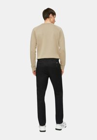 Felpa beige con maniche raglan abbinata a pantaloni neri; tasche posteriori visibili e un accento con logo sulla vita. Sneakers bianche.