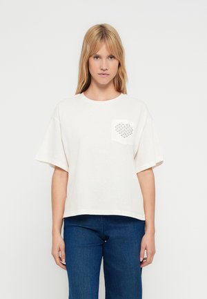 T-shirt color avorio a maniche corte in cotone morbido con una tasca quadrata decorata con un motivo a forma di cuore realizzato con piccoli borchiette d'argento.