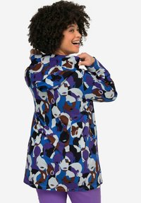 Cazadora de pullover colorida que cuenta con una capucha, hecha de un tejido ligero con un audaz patrón abstracto de cara en púrpura, azul, marrón y blanco.