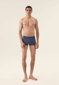 Męskie granatowe szorty kąpielowe wykonane z gładkiego materiału, charakteryzujące się dopasowanym krojem, minimalną długością oraz kontrastowym białym wzorem po bokach.