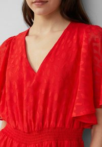 Vrouw in een rode jurk met subtiele dierenprint textuur, V-halslijn, puffed korte mouwen en een cinched tailleband.