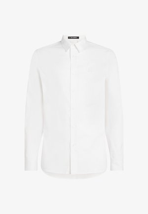 Bílá košile s dlouhým rukávem a knoflíkovým zapínáním, která má klasický límeček a jemně texturovanou látku; obsahuje malé vyšívané logo na hrudi.