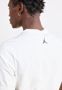 Λευκό βαμβακερό μπλουζάκι με στρογγυλή λαιμόκοψη, με μαύρο λογότυπο Jordan στην επάνω πλάτη, υφαντό ύφασμα και κοντά μανίκια.