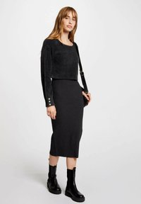 Zwarte gebreide cropped trui met lange mouwen en knoopaccenten, gecombineerd met een aansluitende zwarte rib midi-rok en chunky zwarte enkellaarzen.