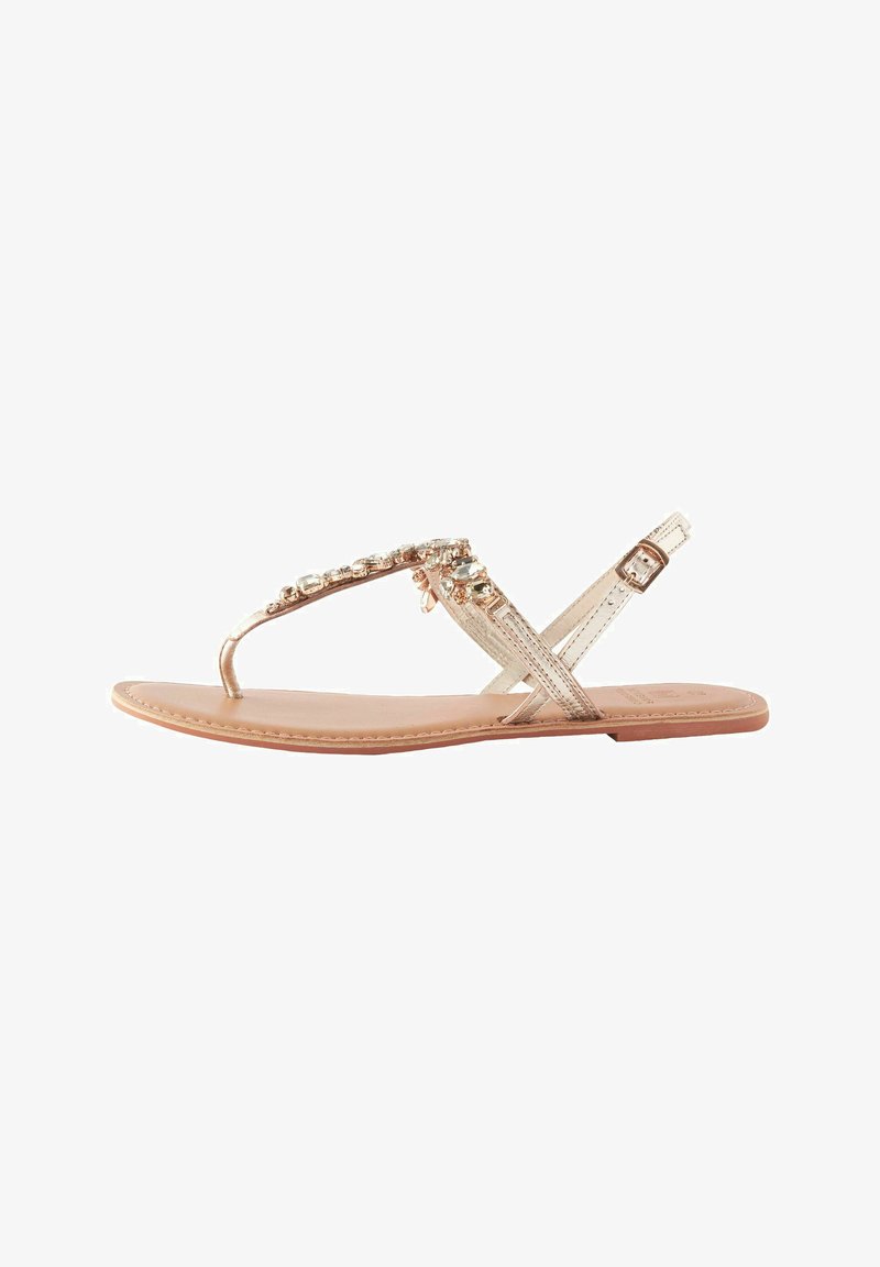 Ploski sandal z medenim zlato odtenkom, okrašen s prozornimi rhinestones na traku in s talno usnjeno podlago v rjavi barvi. Nastavljiv gleženjski trak.