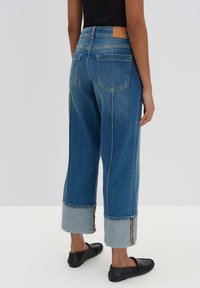 Jeans in denim azzurro chiaro a gamba larga con vita alta, caratterizzati da cuciture a contrasto e orli arrotolati. Patta in pelle sulla parte posteriore della vita.