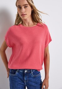 Pull tricoté corail à manches courtes avec un col rond à bords côtes, associé à un jean en denim bleu avec un design à cinq poches et des coutures légères.