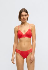 Červená krajková braletka s nastavitelnými ramínky, hlubokým výstřihem do V a hladkým lemem. K tomu odpovídající červené krajkové a síťované kalhotky s ozdobnými detaily.