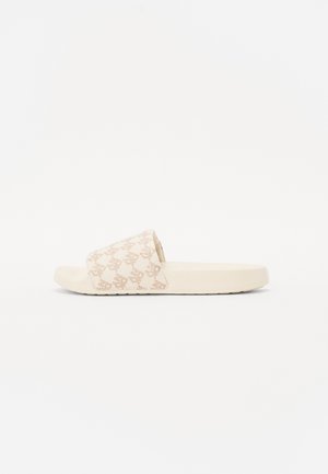 Beige skluzné sandály s širokým páskem a jemným monogramem. Měkký materiál s texturovanou stélkou a plochou gumovou podrážkou.