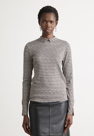 Zwart-witte blouse met lange mouwen, voorzien van een stippenpatroon, een neklap en gestructureerde stof, gecombineerd met een zwarte leren rok.