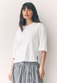 Maglietta bianca a maniche corte con una vestibilità rilassata, abbinata a una gonna a quadretti bianco e nero con tessuto arricciato e vita elasticizzata.