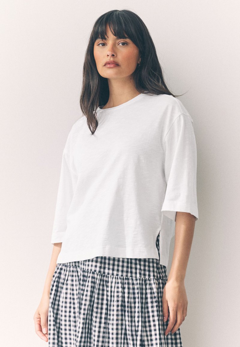 Maglietta bianca a maniche corte con una vestibilità rilassata, abbinata a una gonna a quadretti bianco e nero con tessuto arricciato e vita elasticizzata.