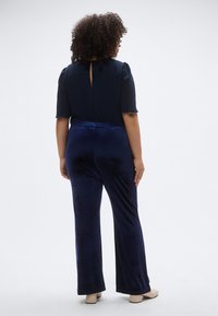 Βελούδινo παντελόνι σκούρου μπλε με άνετη εφαρμογή, συνδυασμένο με μπλούζα σε navy μπλε χρώμα με υφή, κοντά μανίκια και άνοιγμα πίσω με λεπτομέρεια κλειδιού.