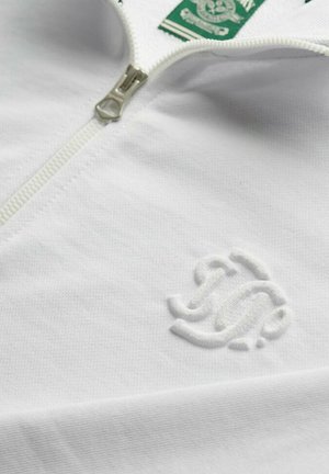 Hvid zip-up sweatshirt med et tekstureret stof, der har et grønt mærke og en subtil broderet logo på forsiden. Lynlåsen er sølvfarvet.