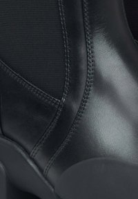 Czarne skórzane botki za kostkę z gładkim wykończeniem, elastycznymi panelami bocznymi i kontrastującymi detalami szycia. Gumowa podeszwa zapewnia trwałość.