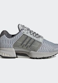 Chaussure de sport grise avec dessus en mesh, panneau de soutien latéral en plastique avec des rayures, fermeture à lacets, semelle rembourrée et semelle extérieure texturée.