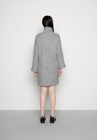 Abito grigio lavorato a maglia con colletto alto, maniche lunghe e vestibilità ampia. Il tessuto ha una trama a coste e arriva fino a metà coscia.