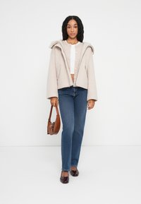 Beige hettejakke med teksturert overflaten, knappelukking, sammen med tettsittende jeans og burgunder flate sko. Brun veske fullfører antrekket.