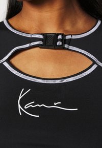 Svart sporttop med en urklippt halsringning, kontrasterande vit sömnad och en framträdande signaturgrafik i vitt på framsidan.