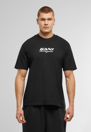 Black cotton T-shirt featuring short sleeves and a crew neckline. Front displays white text: "KANI TheOriginator." Simple design, relaxed fit.
