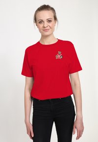 Red cotton t-shirt with short sleeves featuring a cartoon graphic of three characters and a heart on the chest area. Black jeans worn.