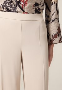 Pantaloni beige su misura con una texture liscia, dotati di tasche laterali e un design pulito e semplice. La vita è piatta senza chiusure visibili.