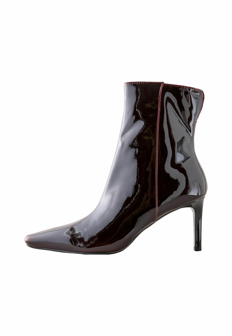 Skinnende sorte ankelstøvler med spids tå, slank høj hæl og kontrasterende rød syning langs sømmen. Glat, skinnende lakfinish.
