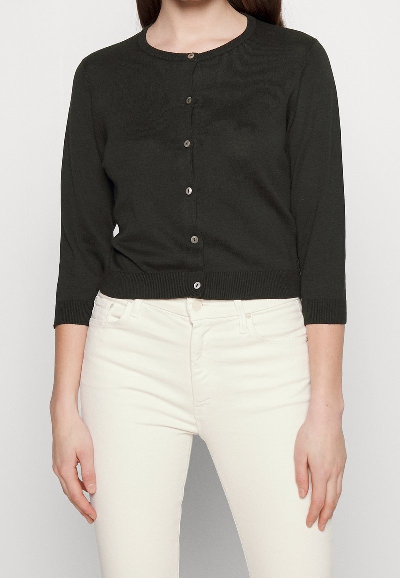 Dunkelgrüner Cardigan mit rundem Halsausschnitt, sieben Knöpfen auf der Vorderseite und Dreiviertelärmeln. Rippstruktur am Saum und an den Manschetten.