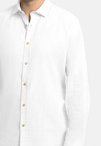 Camisa blanca de manga larga hecha de una tela texturada, con cuello abotonado, botones de madera y un diseño de ajuste relajado.