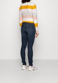 Blaue Slim-Fit-Jeans mit einer dunklen Waschung werden mit einem mehrfarbigen gestreiften Pullover kombiniert, der gelbe, rosa, graue und weiße horizontale Streifen aufweist.
