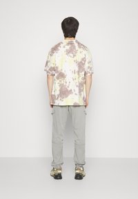 Överdimensionerad tie-dye-t-shirt i gula och bruna nyanser, kombinerad med grå cargobyxor och svarta sneakers med gröna detaljer.