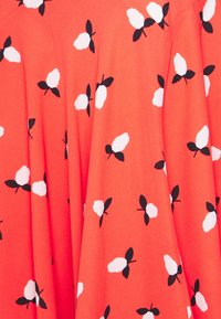 Koralstoff mit einem Blumenmuster aus weißen Blumen und schwarzen Blättern, mit Falten für Textur und Bewegung.