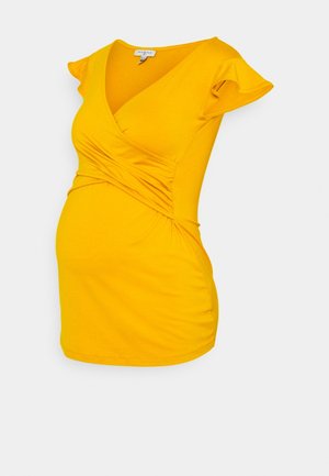 Gele zwangerschapsblouse met korte, gerafelde mouwen, v-hals en geplooide zijdetails voor een aansluitende look. Zachte, rekbare stof.