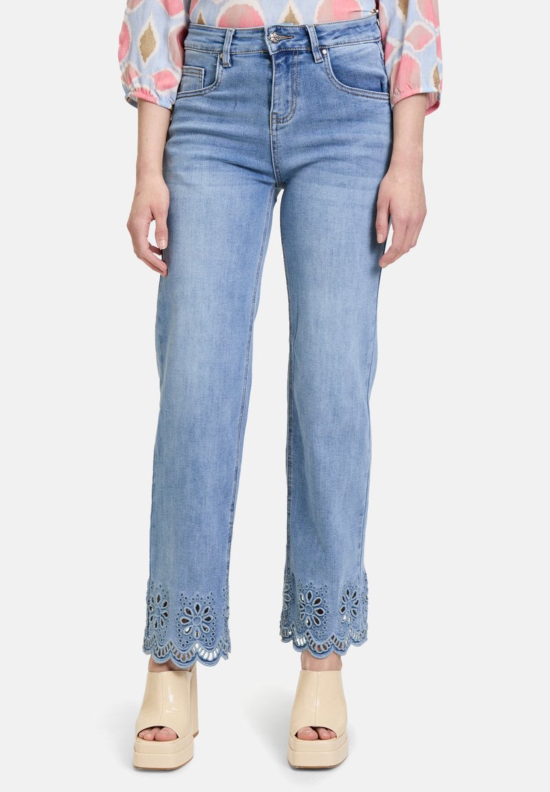 Jean en denim bleu clair cropped avec un ourlet festonné et des broderies florales. Associé à des chaussures à plateforme beiges.