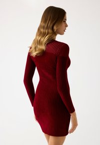 Abito lungo a maniche lunghe rosso con silhouette aderente, caratterizzato da righe orizzontali e verticali a contrasto e un tessuto strutturato.