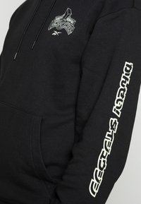 Svart hoodie i bomullsblandning, med en grafisk logotyp på bröstet och text längs ärmen i vitt. Inkluderar en framsida ficka.