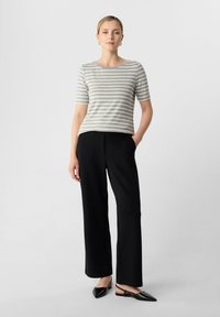 Grau-weiß gestreiftes T-Shirt mit kurzen Ärmeln, kombiniert mit schwarzen weit geschnittenen Hosen und schwarzen Slingback-Schuhen. Einfaches Design, lässige Passform.