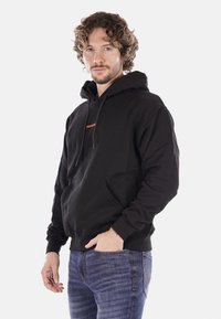 Felpa con cappuccio nera in misto cotone. Presenta una tasca a marsupio sul davanti e un logo arancione sul petto. Texture liscia, vestibilità rilassata.