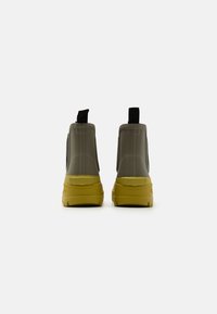 Bottines en cuir gris imperméables avec une finition texturée, dotées d'une semelle jaune et d'une languette. Le design est élégant avec des bords arrondis et des accents minimalistes.