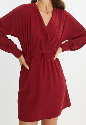 Rode rekbare stoffen jurk met V-hals, lange mouwen, geplooide taille en losse pasvorm. De textuur is glad met een lichte glans.