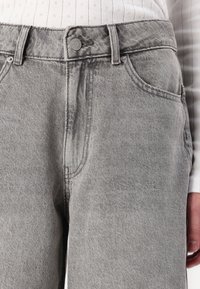 Harmaat farmarit korkealla vyötäröllä, klassinen viiden taskun muotoilu ja etupainike. Pehmeä, tekstuuriinen kangas, jossa on hienovarainen haalistuma.