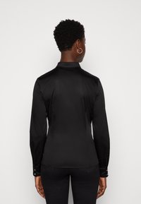 Schwarzes Langarmshirt mit glatter Textur, maßgeschneiderter Passform und klassischem Kragen. Verfügt über geknöpfte Manschetten und ein elegantes, minimalistisches Design.
