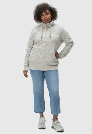 Light gray zip-up hoodie with a high collar, featuring a scattered pattern of small colored dots, paired with blue cropped jeans and sneakers.