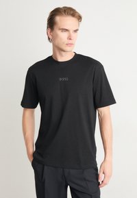T-shirt en coton noir avec col rond et manches courtes, comportant un logo "BOSS" en relief au centre de la poitrine. Tissu lisse et texturé.