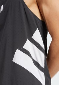 Débardeur de sport noir avec une texture perforée. Présente un design distinct à rayures blanches sur le côté, mettant en valeur des matériaux contrastants.