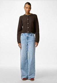 Brūns īss kardigāns ar pogu aizdari, kombinēts ar gaiši zilām plaša griezuma džinsām un bordo apaviem. Visā virsmā gluda tekstūra.